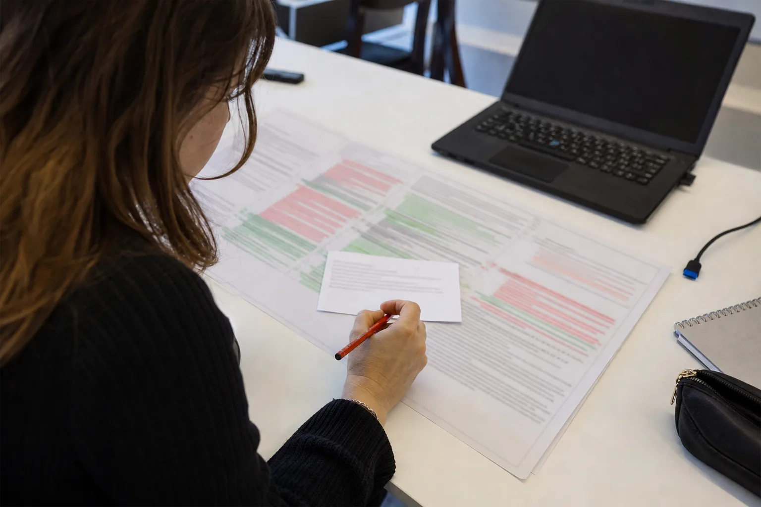 A short typed summary card resting on top of a long printed diff, a red pencil underlining one line